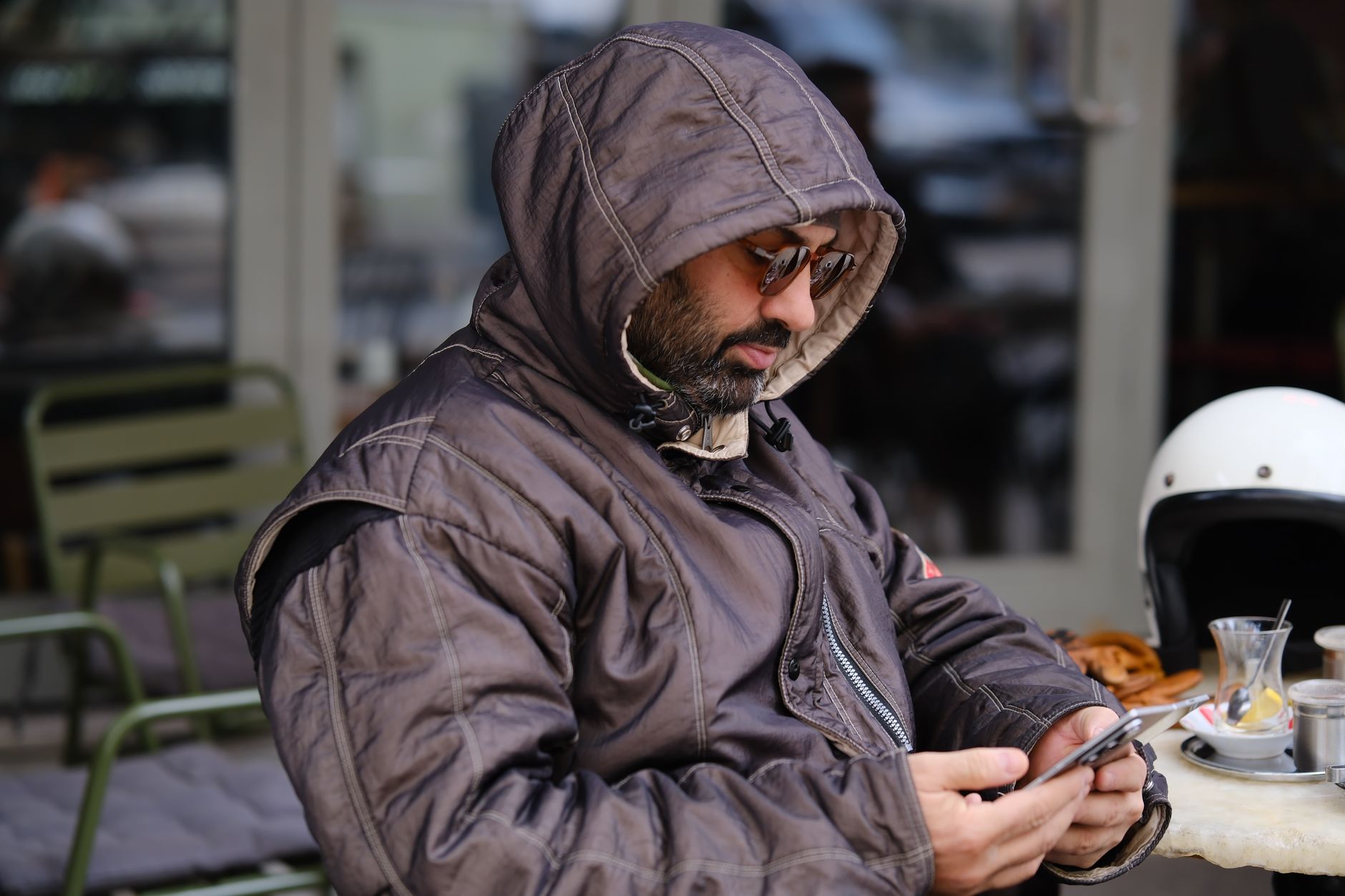Hombre con capucha y gafas de sol consultando el móvil en la terraza de un café